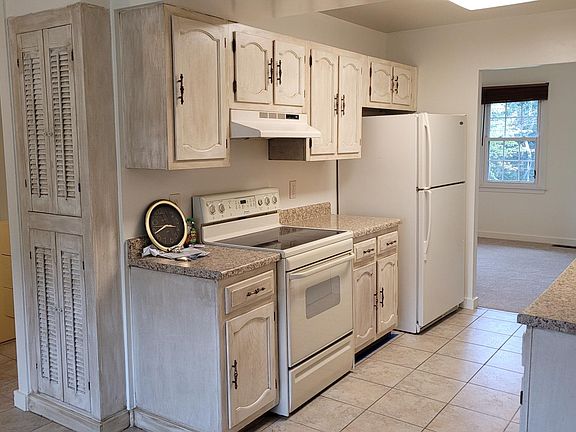 Left side of the kitchen with built-in spice cabinets, electric stove, external venting over range fan, large refrigerator.