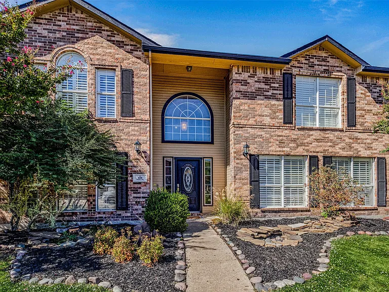 Brick facade residence featuring a prominent arched entry window, decorative shutters, and a concrete pathway