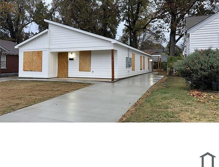 Single-story white home with a new concrete driveway and a clean exterior. The property is currently secured with boarded windows and doors.