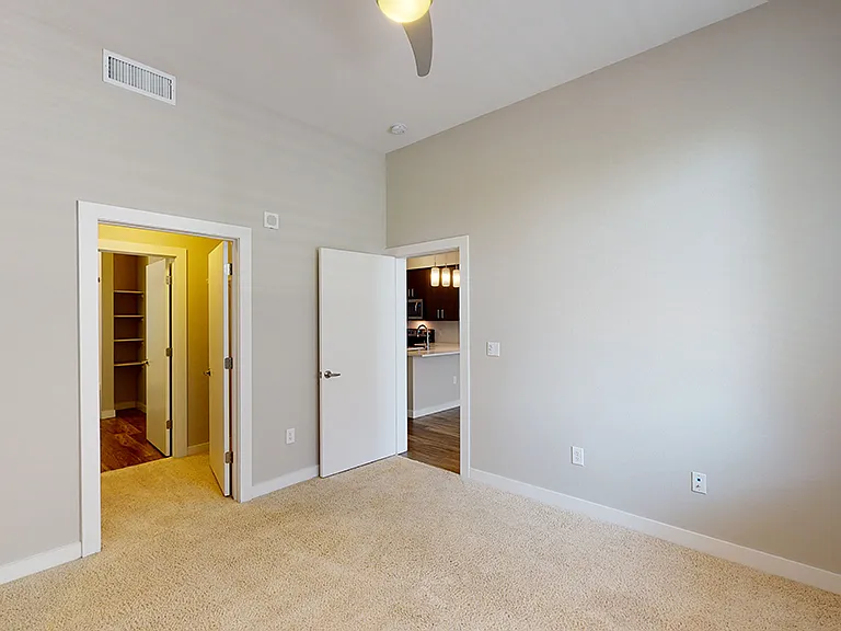 Spacious apartment bedroom with large closet, attached bathroom and plush carpet flooring.