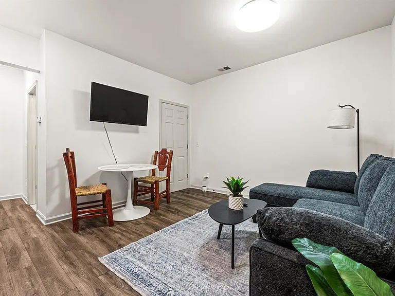 Open living area with sectional seating, mounted TV, and a compact dining nook on durable wood-look flooring.