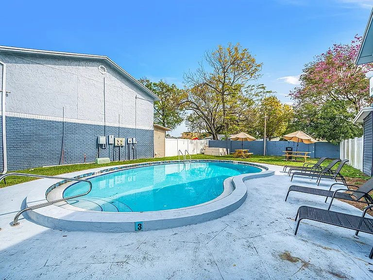 Inviting outdoor pool area with comfortable lounge chairs and shaded picnic tables, perfect for relaxation.