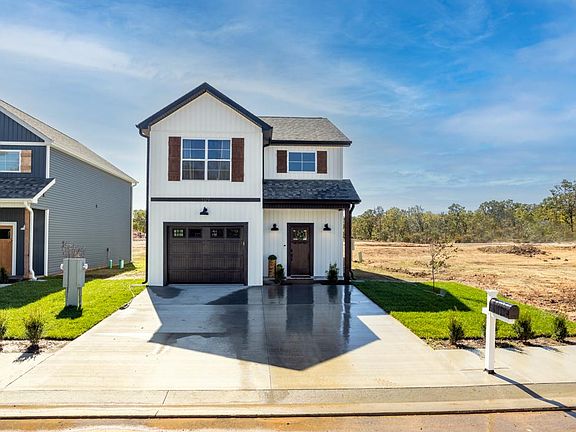 The exterior of Pinnacle Place townhomes features modern siding with a neutral color palette, attached garage, driveway and mailbox, large windows, and a charming front porch.