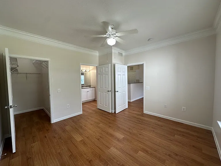 Inviting bedroom with wood-style flooring, spacious closet, and attached bathroom, enhanced by neutral tones and natural light. Inviting bedroom with wood-style flooring, spacious closet, and attached bathroom, enhanced by neutral tones and natural light.
