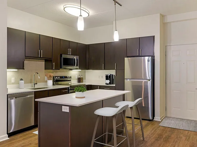 Renovated Package I kitchen with white quartz countertops, espresso cabinetry, stainless steel appliances, tile backsplash, and hard surface flooring throughout (in select homes)