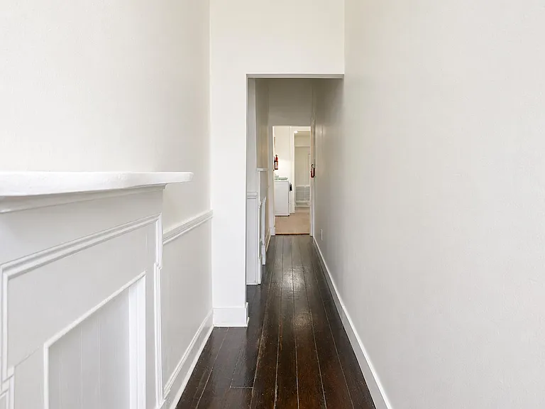 Long interior hallway with white walls, decorative wainscoting, and dark wood floors leading to the home's main areas.