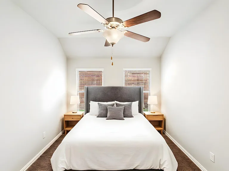 Vaulted ceiling bedroom featuring a ceiling fan with light fixture, two windows with blinds, and brown carpet flooring