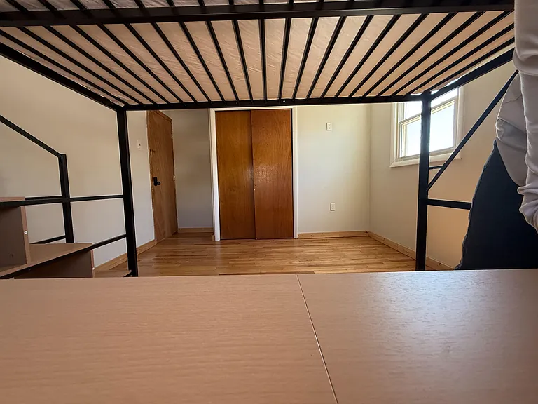 Bedroom with a loft-style bunk/metal frame, wood-look flooring, closet doors, and a window for natural light.