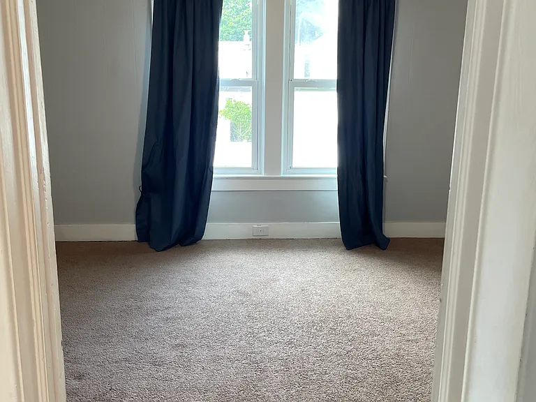 This bedroom offers great natural light, soft carpeting, and a comfortable layout perfect for a bedroom, guest room, or office space.