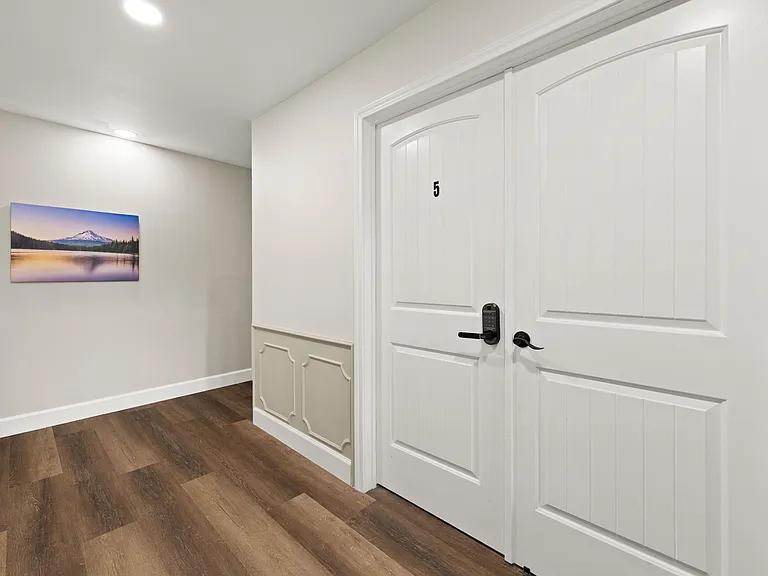 Wide hallway with durable wood-look flooring, crown molding, and secure keyed entry doors for added privacy.