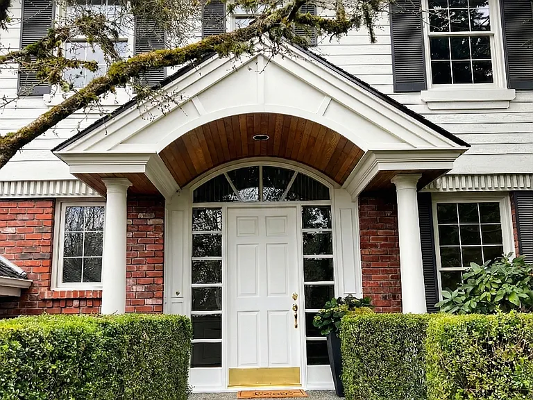 The vaulted portico with wood soffit/paneling is a high-end custom touch that adds warmth and luxury to the white exterior