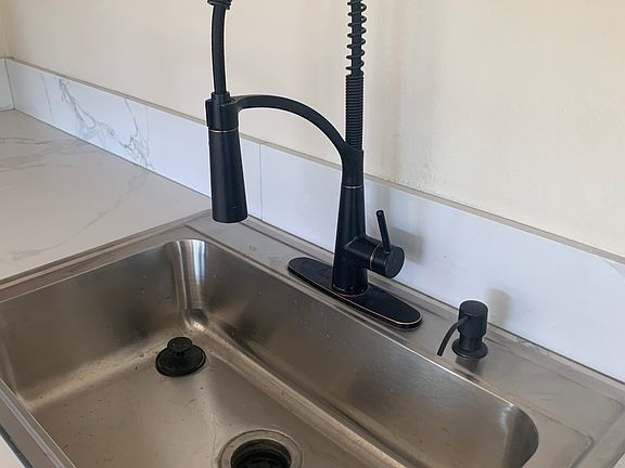 Close-up of kitchen faucet and stainless steel sink. Includes soap dispenser and garbage disposal (not in photo).