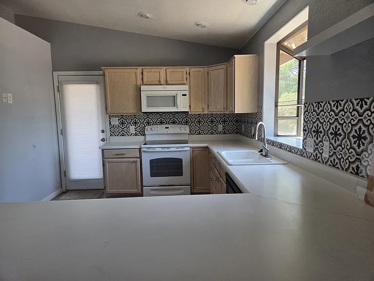 Large kitchen with lots of cabinets, dishwasher, door leading out to the shaded deck.