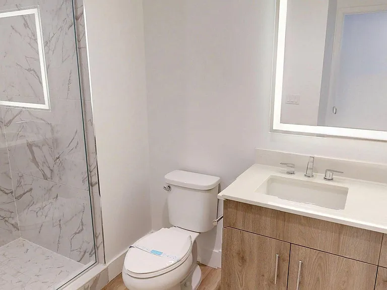 Apartment Bathroom with glass enclosed shower, LED vanity mirror and Wood Style Flooring.