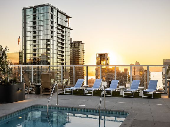 Luxurious rooftop pool with sun loungers and breathtaking skyline views at sunset, perfect for relaxation.