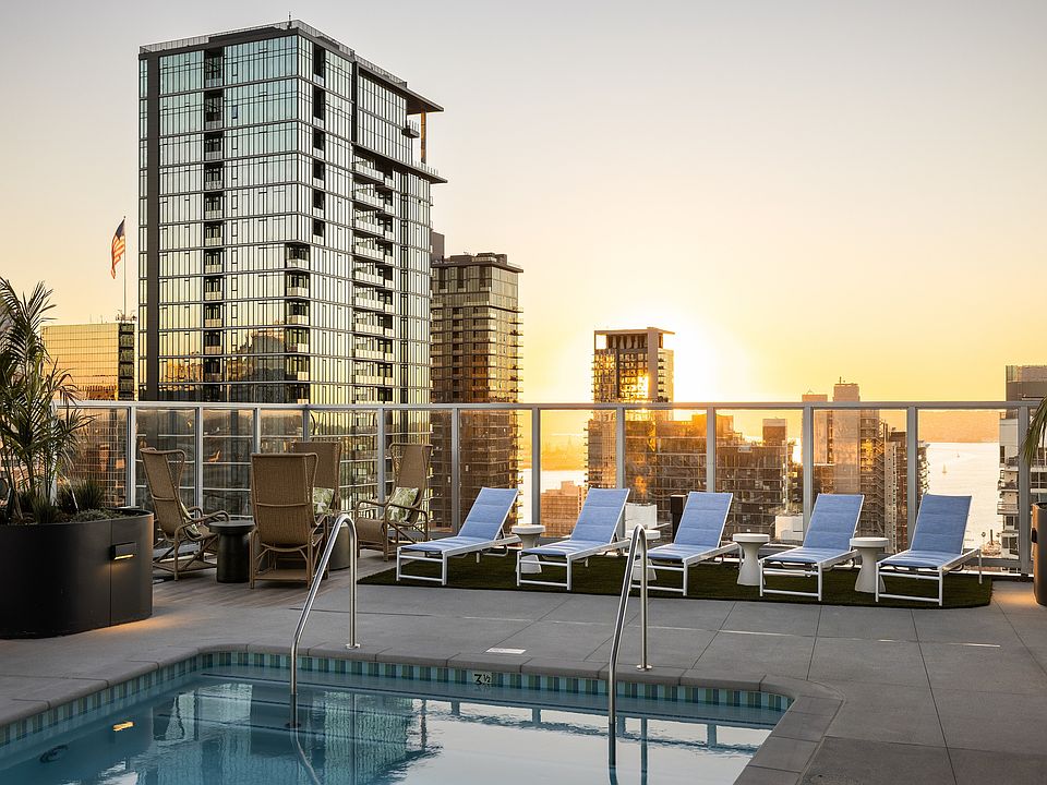 Luxurious rooftop pool with sun loungers and breathtaking skyline views at sunset, perfect for relaxation.