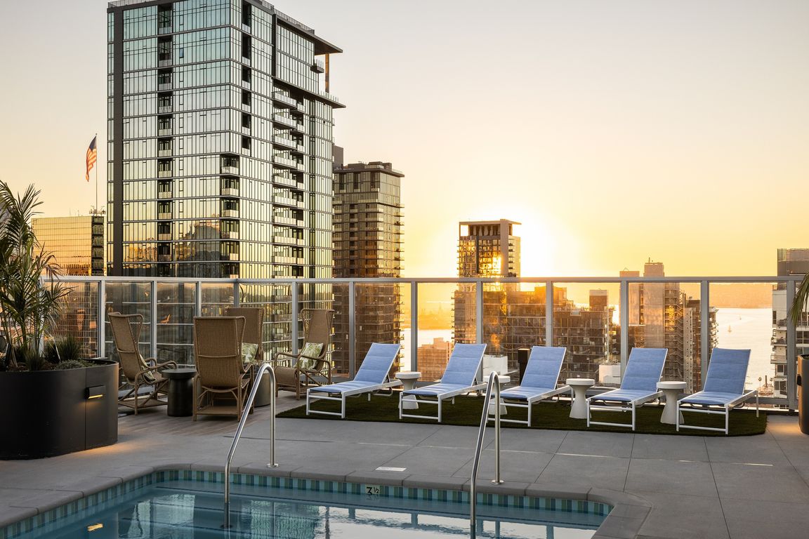 Luxurious rooftop pool with sun loungers and breathtaking skyline views at sunset, perfect for relaxation.