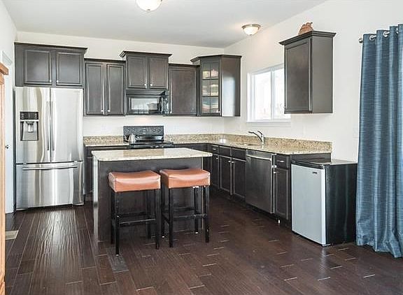 Handscraped Wood Flooring-Center Island with Breakfast Bar-Staggered Cabinetry-Glass Front-Crown Molding-Granite-Stainless Appliances-Brushed Nickel Hardware-Walk In Pantry