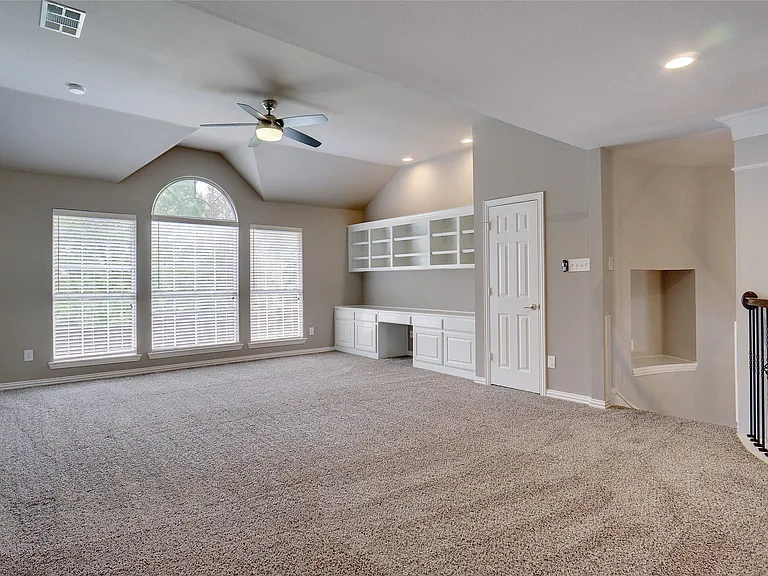 Spacious secondary living area featuring vaulted ceilings, three large windows with an arched transom, a built-in desk with cabinetry, and recessed lighting