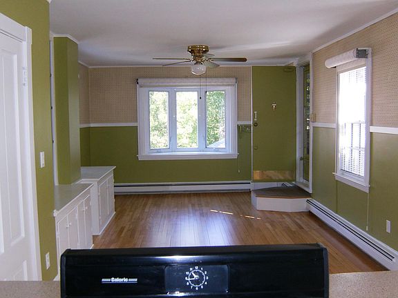 Replaced this stove sticking up in picture with new stove that is even with the counter top; looking into living room from kitchen, screened in porch up step at far right; kitchen closet to immediate left; entertainment center beyond.