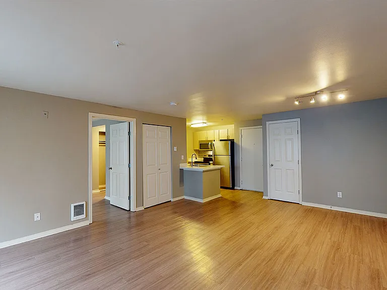 Apartment kitchen with stainless steel appliances, dining and living room with wood-style flooring.
