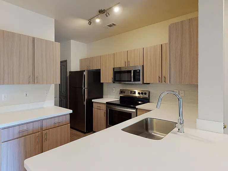 Apartment kitchen with stainless steel appliances, quartz countertops and wood-style flooring.