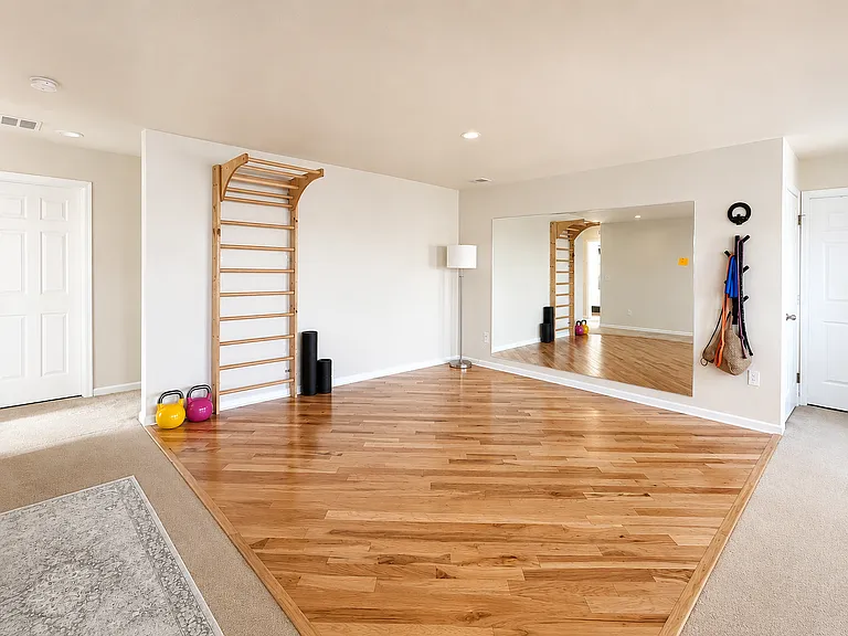 Shared upstairs fitness loft with hardwood exercise area, wall mirror, wall bars and fitness equipment. Digitally enhanced for presentation.