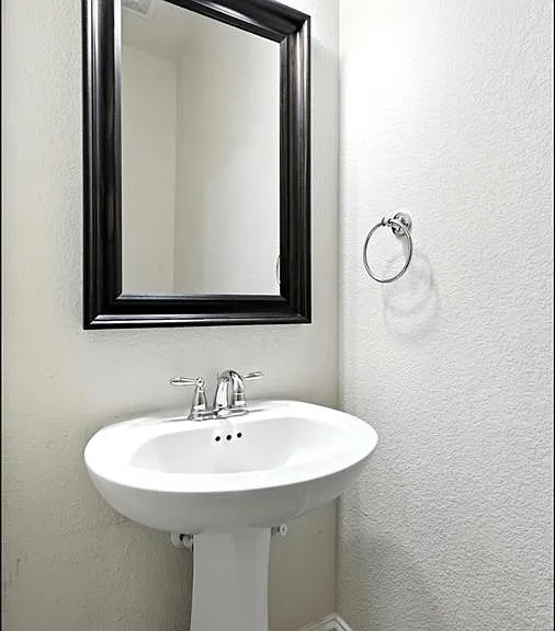 Pedestal sink with chrome fixtures, framed mirror, and wall-mounted towel ring
