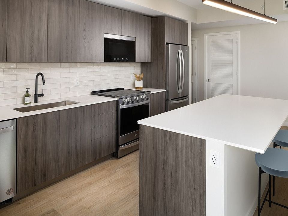 Upgrade Collection II Three-bedroom apartment kitchen with espresso cabinetry, white tile backsplash, white quartz countertop, and hard-surface vinyl plank flooring