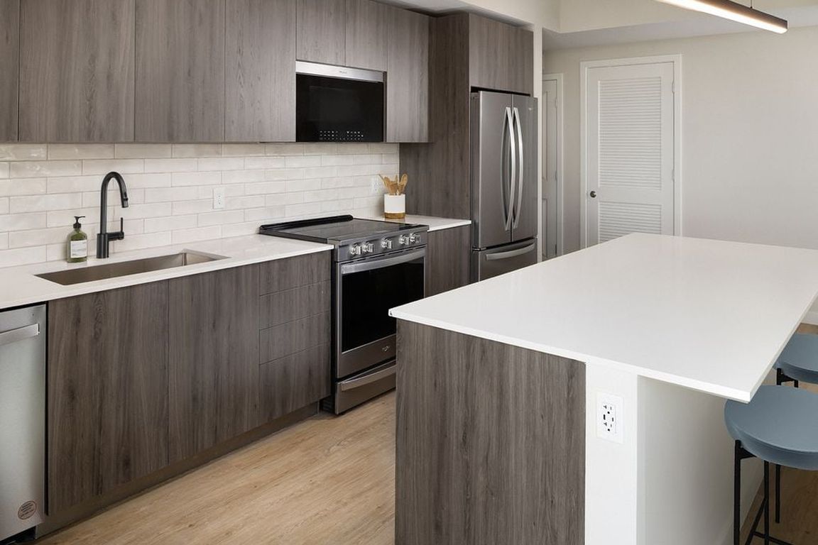 Upgrade Collection II Three-bedroom apartment kitchen with espresso cabinetry, white tile backsplash, white quartz countertop, and hard-surface vinyl plank flooring