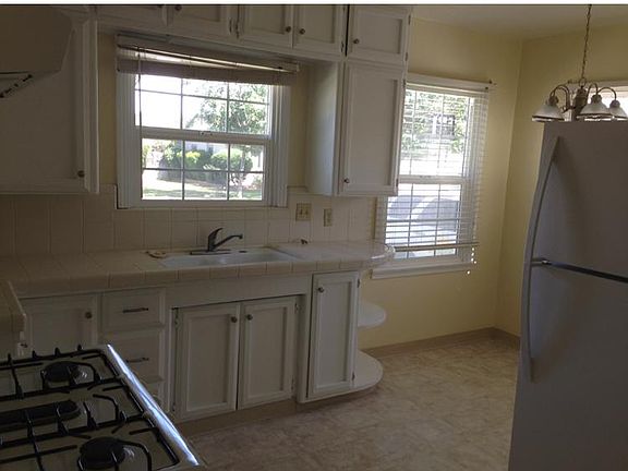 Light filled kitchen including refrigerator, tile counters, gas stove, garbage disposal, and eat in dinette area.