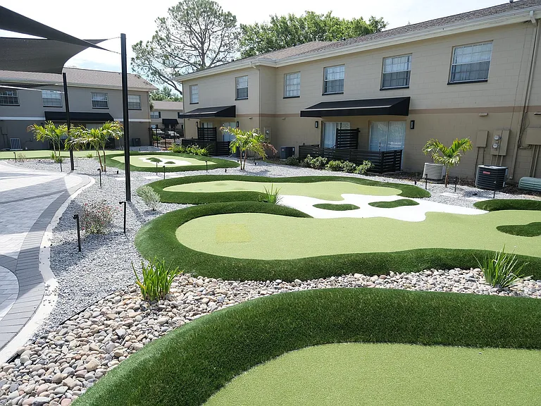 Charming apartment complex featuring a beautifully landscaped mini-golf course surrounded by lush greenery and pebbled pathways.