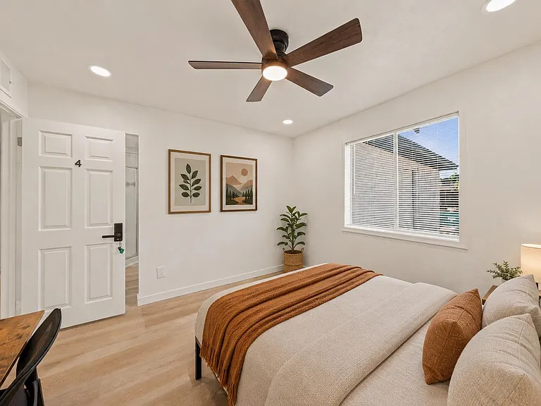 Spacious bedroom with ceiling fan, recessed lighting, and a large window with blinds; includes a desk area for work or study.