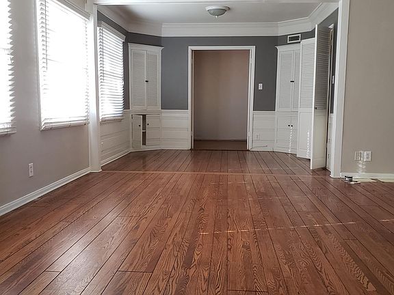 A large living room with high beam ceiling, fireplace and mantel. Beyond the living room is the dining room with 4 built in cabinets. Pictured in the far back of this photo is a room for an office or fourth bedroom. Not shown are 2 doors to that office/b