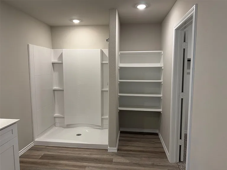 Walk-in shower with integrated shelving, recessed lighting, and wood-finish
 flooring