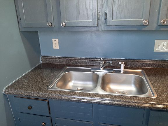 Kitchen sink with bank of cupboards above and below; bathroom door is to left