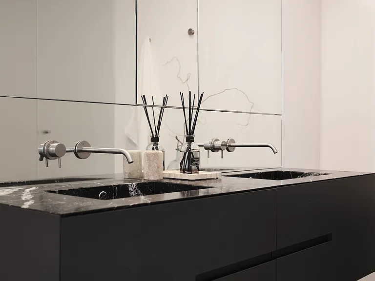 Sleek Double Vanity with Contemporary Finishes_ This refined bathroom features a custom floating vanity with integrated black stone sinks, wall-mounted fixtures, and a seamless mirrored backdrop.