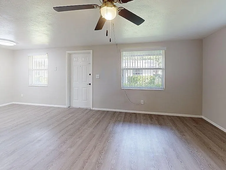 Bright and airy living room featuring elegant wood flooring, large windows, and a modern ceiling fan.