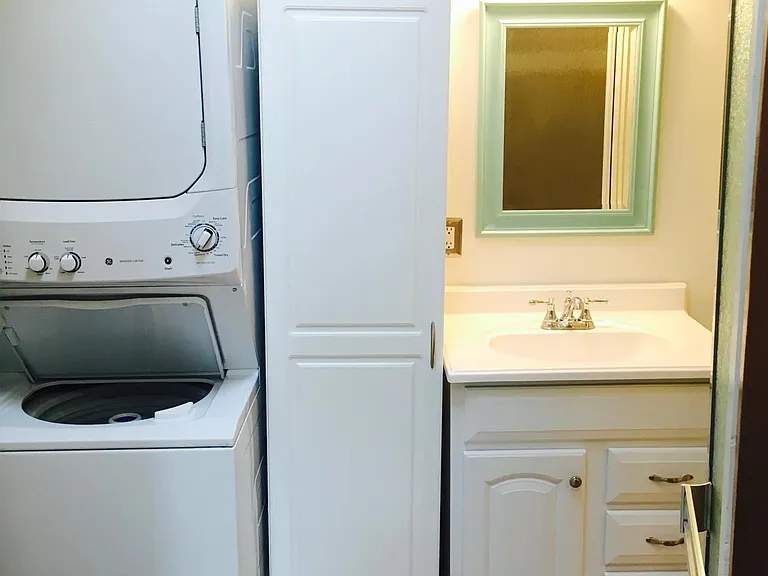 Stacked washer/dryer in bathroom with linen cabinet.