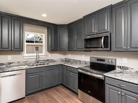 Kitchen with stainless steel appliances, gray cabinets, light wood-style floors, light stone counters, and recessed lighting