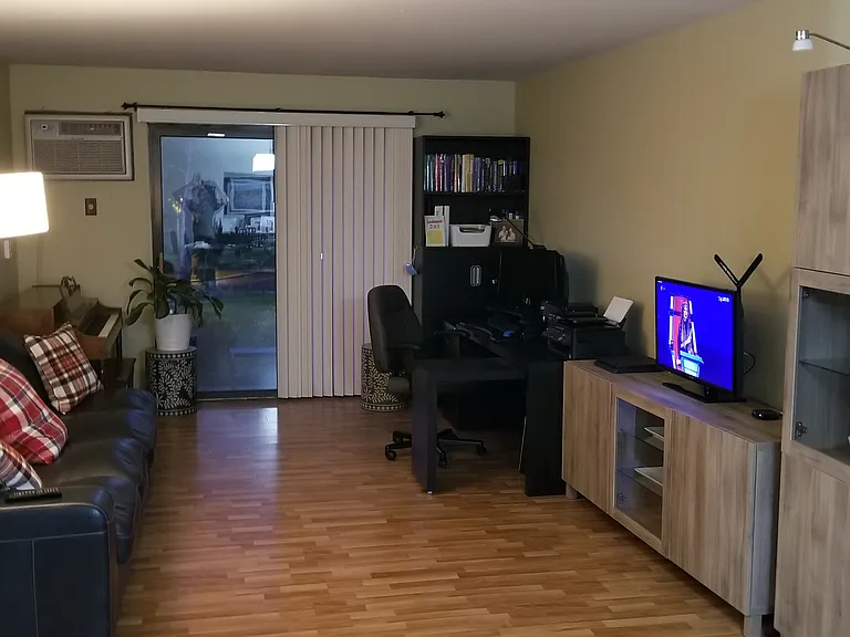 Large living space open to the dining area. Air conditioner and outdoor access can be seen at the back end.
