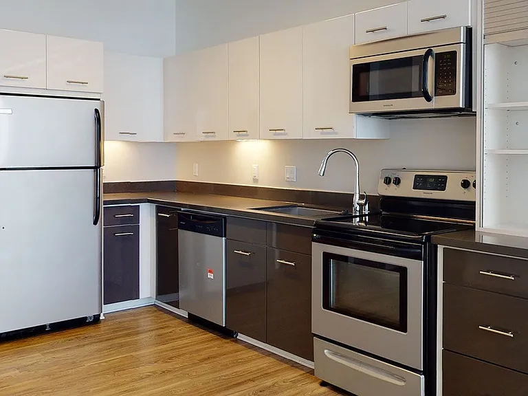 Apartment kitchen with stainless steel appliances, quartz countertops and wood-style flooring.