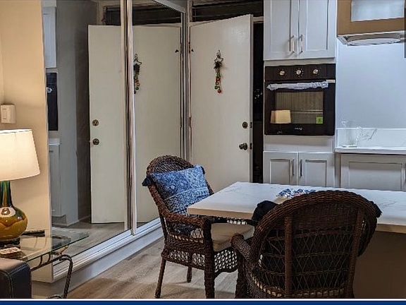 Standing in living room, looking toward the kitchen front door entrance. On left, the kitchen pantry with large mirrored double doors.