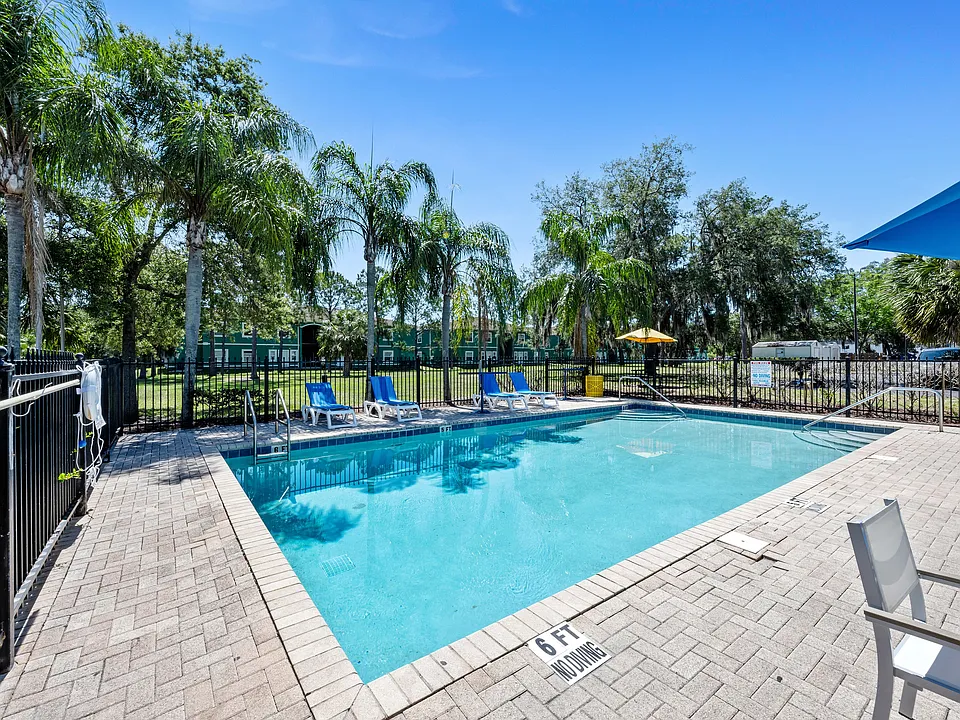 Inviting outdoor pool area with sun loungers and lush palm trees under a clear blue sky, offering a perfect relaxation spot.