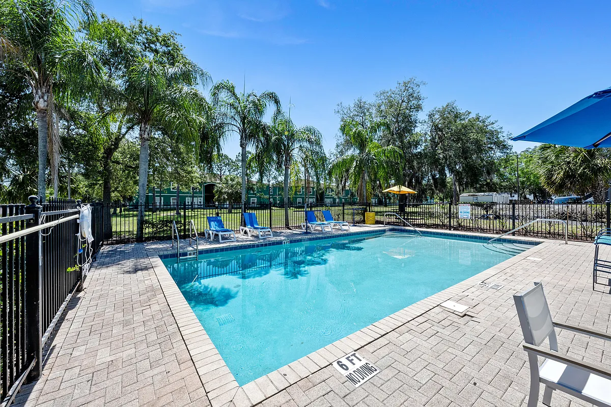 Inviting outdoor pool area with sun loungers and lush palm trees under a clear blue sky, offering a perfect relaxation spot. - Vista Palms