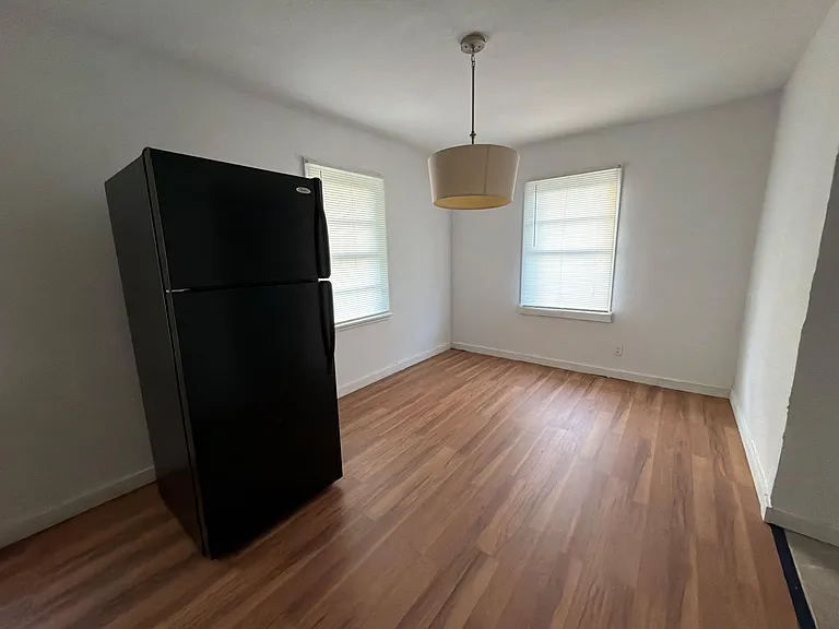 Open dining area with wood-style flooring, two windows with blinds, and an overhead pendant light for everyday meals.