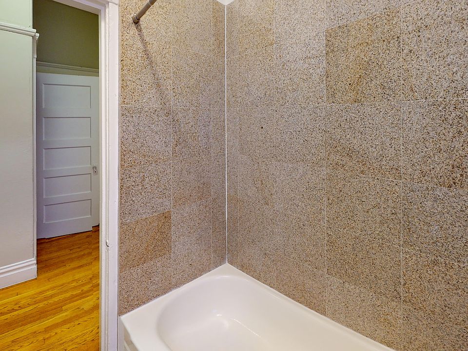 A spacious shower with tiled walls and a bathtub, leading to a door that opens to another room.