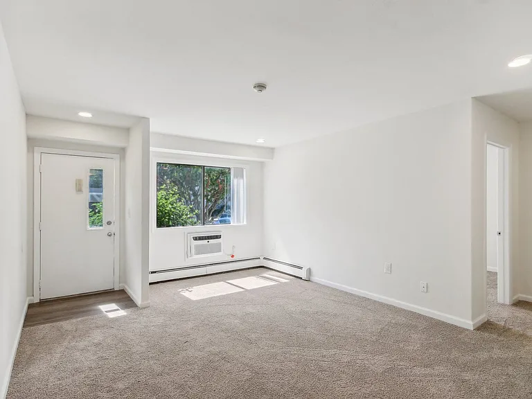 a view of living room with white walls and a window, front door and bedroom entrance