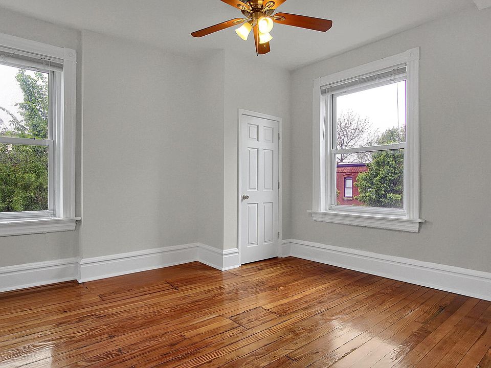 Primary bedroom with tall ceilings, salvaged hardwood floors, large windows, ample closet storage, and a ceiling fan for year-round comfort.