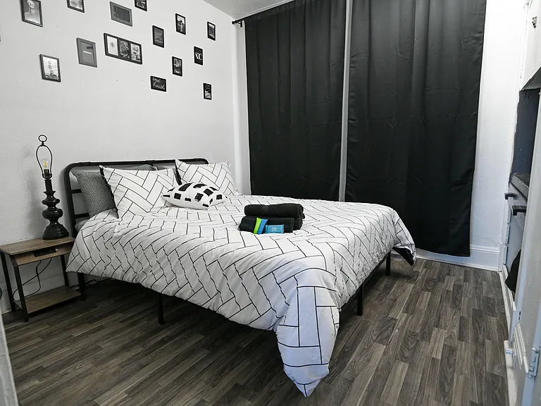 Furnished bedroom with a full bed, nightstand, and wall art, plus blackout curtains and durable wood-look flooring.